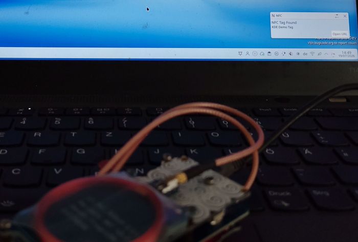 Photo with Proxmark3 in the lower left corner placed on the NFC reader of a laptop, on the screen of which a notification is displayed.